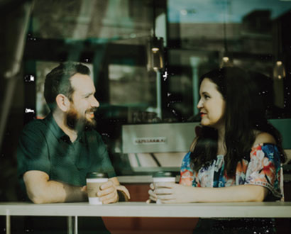 A man and woman facing each other in a coffee shop window - Relatives & Friends Programme Image